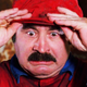 Bob Hoskins in the Super Mario Bros. movie is grabbing his red hat and looking despairing.